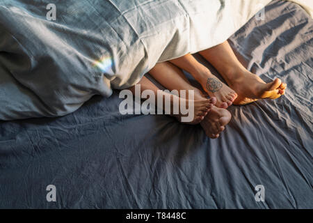 Die Paar Füße unter Bettdecke im Bett Stockfoto