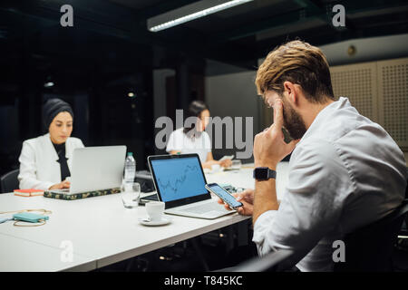 Geschäftsfrau auf Laptops und Smartphones am Konferenztisch Stockfoto