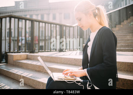 Junge Frau sitzt auf der Stadt Treppe Tippen auf Laptop Stockfoto
