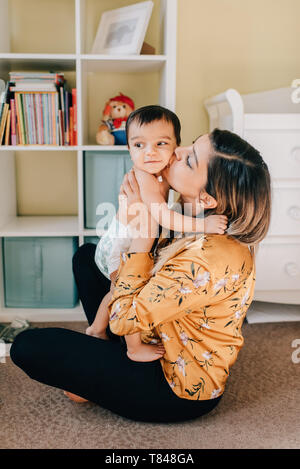 Mutter sitzt auf Kindergarten Boden küssen Baby Sohn Stockfoto