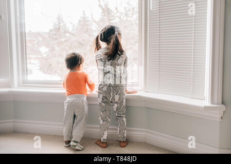 Mädchen und Bruder durch Wohnzimmer Fenster suchen, Ansicht von hinten Stockfoto