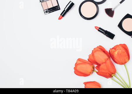 Flach Anordnung von Frauen Kosmetik, Make-up Zubehör und Bouquet von roten Tulpen auf weißem Hintergrund mit Kopie Raum, Ansicht von oben. Stockfoto