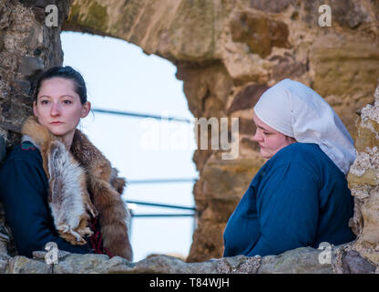 Tag des Mittelalters. Dirleton Castle, East Lothian, Schottland, Vereinigtes Königreich, 11. Mai 2019. Historische Umfeld Schottland Familientag Historische Re-enactment der mittelalterlichen Schlachten von Menschen in mittelalterlichen Kostüm aus der Historischen Saltire Society gekleidet. Frauen gekleidet in mittelalterlichen Kostüm beobachten Sie die Leistung aus einer Burgruine Fenster Stockfoto