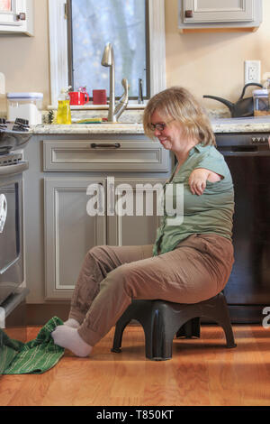 Frau mit TAR-Syndrom herauf ein Küchentuch mit ihren Füßen Stockfoto