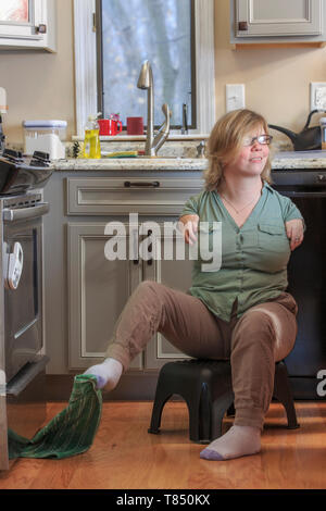 Frau mit TAR-Syndrom herauf ein Küchentuch mit ihren Füßen Stockfoto