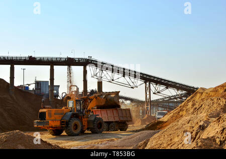 Rad Frontlader entladen Sand in schweren Dump Truck. Crushing Fabrik, Maschinen und Anlagen für die Zerkleinerung, Schleifen Stein, Sortieren, Sand und b Stockfoto