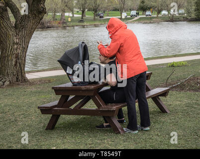 Zwei Frauen und ein Kleinkind im Park in Stratford, Ontario. Einer von ihnen nimmt ein Bild des Kleinkindes. Cool grauer Tag. Stockfoto