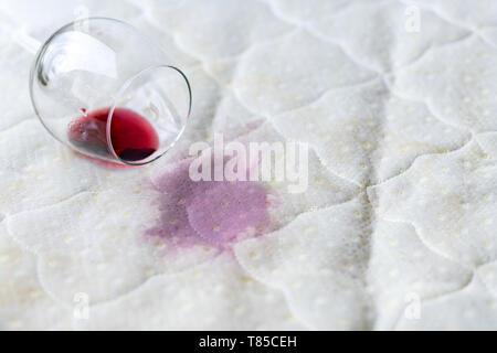 Wein Glas verschüttet auf dem Bett. Fallengelassen Weinglas auf weißen Bettlaken. Rosa nassen Fleck. Pech, unglückliche Situation. Stockfoto