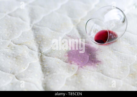 Wein Glas verschüttet auf dem Bett. Fallengelassen Weinglas auf weißen Bettlaken. Rosa nassen Fleck. Pech, unglückliche Situation. Stockfoto