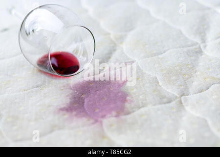 Wein Glas verschüttet auf dem Bett. Fallengelassen Weinglas auf weißen Bettlaken. Rosa nassen Fleck. Pech, unglückliche Situation. Stockfoto