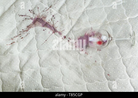 Wein Glas verschüttet auf dem Bett. Fallengelassen Weinglas auf weißen Bettlaken. Rosa nassen Fleck. Pech, unglückliche Situation. Stockfoto