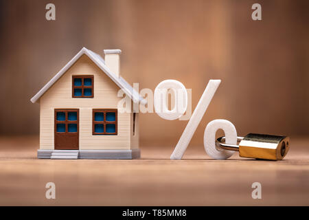 Haus Modell in der Nähe von Prozentzeichen mit Tastensperre über Holz- Schreibtisch Stockfoto