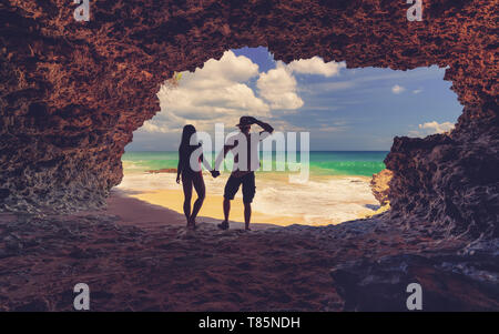 Indonesische verliebtes Paar sitzen in einer Höhle auf dem tropischen Strand auf Hintergrund tobenden Wellen im Meer und blauer Himmel Stockfoto