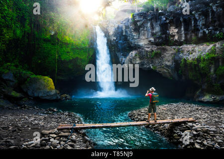 Aktiven Lifestyle und Travel Concept: Travel Backpacker mit Kamera in der Hand Foto machen bei Sonnenaufgang erstaunliche Wasserfall im tropischen Dschungel versteckt. Stockfoto