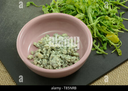 Blauschimmelkäse in Rosa und argula Gewürzkraut Schüssel Salat Blätter auf schwarz Schneidbrett auf sackleinen Stockfoto