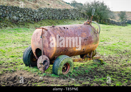 Eine rostige, korrodierte slurry Tanker mit platten Reifen sitzt in ein schlammiges Feld in der irischen Landschaft aufgegeben. Stockfoto