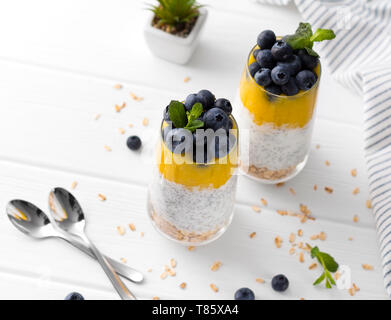 Zwei Gläser von Chia Pudding mit Blaubeeren, mango Mousse und Hafer Müsli auf dem Küchentisch. Stockfoto