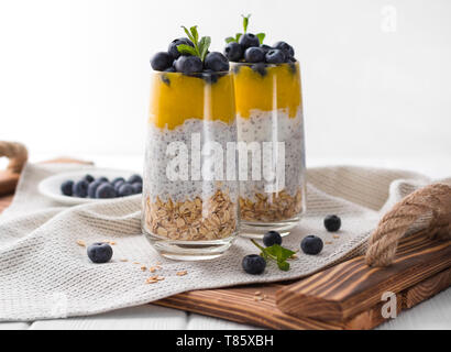 Glas Joghurt mit Blaubeeren und Mango Mousse, Chia Samen und Haferflocken auf einer hölzernen Fach. Stockfoto