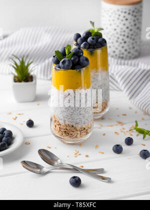 Zwei Gläser von Chia Pudding mit Blaubeeren, mango Mousse und Hafer Müsli auf dem Küchentisch. Stockfoto