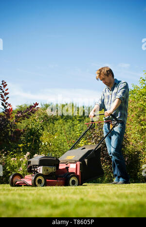 Junger Mann mäht den Rasen an einem sonnigen Frühlingstag Stockfoto