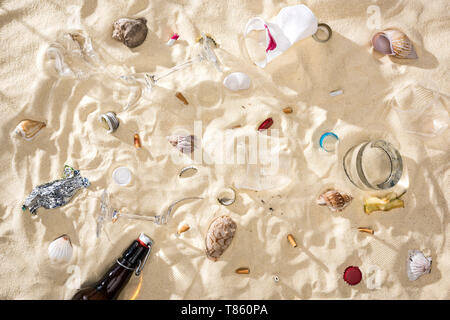 Blick von oben auf die seashells, Glasflasche, verstreute Zigarettenkippen, zerbrochene Gläser, Apple Core, Plastikbecher und Candy wrapper auf Sand Stockfoto