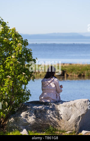 Junge Mädchen auf einem Stein saß im Schatten eines Baumes über nach Vancouver Island suchen Stockfoto