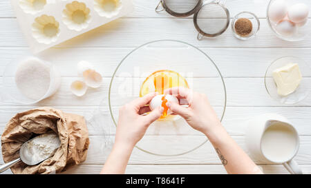 7/8-Ansicht von Frau Risse Ei in der Schüssel beim Kochen am Tisch Stockfoto