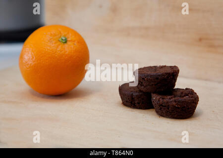 Eine orange und eine kleine von Brownies zusammen Stapel auf eine Küche Schneidbrett Stockfoto