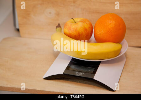 Ein Apfel, Banane und Orange auf einer digitalen Waage gewogen werden Stockfoto