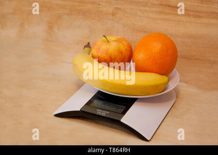Banane, Orange und Apfel auf einem digitalen Maßstab als eine gesunde Wahl wiegen Stockfoto