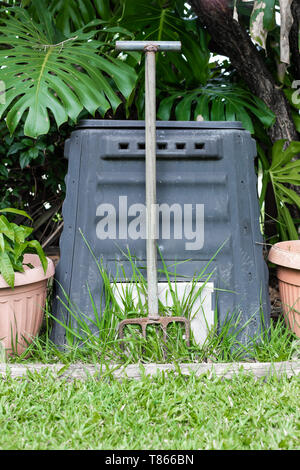 Eine Komposttonne und Pitch Gabel in einer australischen Garten im Hinterhof, die von Pflanzen und grünes Gras umgeben Stockfoto