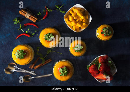 Traditionelle italienische süßes Dessert Panna cotta mit Mango Gelee serviert in Töpfen und mit frischen echten strawberrries und Minze verschönert. Dunkelblau backgr Stockfoto