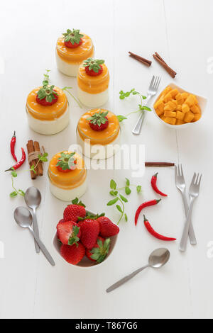 Traditionelle italienische süßes Dessert Panna cotta mit Mango Gelee mit Hauch von red hot chili Piri-Piri in Töpfen auf weissem Holztisch und embellis serviert. Stockfoto