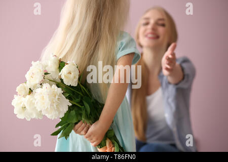 Süße kleine Mädchen verstecken Blumenstrauß für Mutter hinter ihrem Rücken auf farbigen Hintergrund Stockfoto