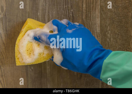 Mann hält gelben Schwamm in der Hand und säubert einen gefliesten Wand in Holz. Stockfoto