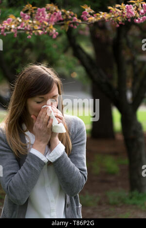 Tausendjährige Frau Niesen im Park umgeben von Blumen - es sieht aus wie Allergien! Stockfoto