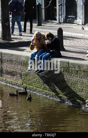 Touristen Fütterung Enten auf Oudezijds Achterburgwal Kanal in Amsterdam, Niederlande Stockfoto
