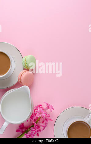 Tasse Kaffee mit Milch, Makronen, Milch Glas auf Pastell rosa Hintergrund mit muscari und Hyazinthen Blumen dekoriert. Von oben nach unten, flach. Romantische morni Stockfoto