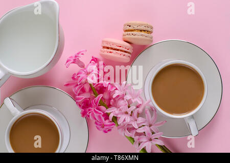 Tasse Kaffee mit Milch, Makronen, Milch Glas auf Pastell rosa Hintergrund mit muscari und Hyazinthen Blumen dekoriert. Von oben nach unten, flach. Romantische morni Stockfoto
