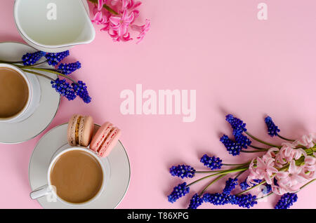 Tasse Kaffee mit Milch oder Latte, Makronen und Milch Glas auf Pastell rosa Hintergrund mit muscari und Hyazinthen Blumen dekoriert. Von oben nach unten, flach. De Stockfoto