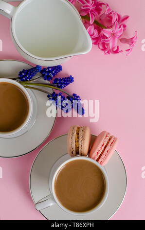 Tasse Kaffee mit Milch oder Latte, Makronen und Milch Glas auf Pastell rosa Hintergrund mit muscari und Hyazinthen Blumen dekoriert. Von oben nach unten, flach. De Stockfoto