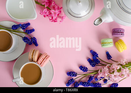 Tasse Kaffee mit Milch oder Latte, Makronen und Milch Glas auf Pastell rosa Hintergrund mit muscari und Hyazinthen Blumen dekoriert. Von oben nach unten, flach. De Stockfoto