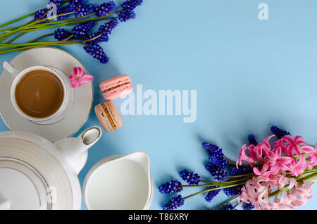 Romantisches Frühstück Konzept. Tasse Kaffee mit Milch, Makronen, Milch Glas auf Pastell-blaue Hintergrund mit muscari und Hyazinthen Blumen dekoriert. Nach oben Stockfoto