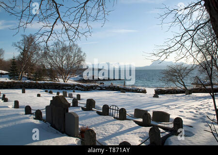 Norwegen Trondenes, Friedhof im 13. Jahrhundert mittelalterliche Kirche mit Bucht im Hintergrund Stockfoto