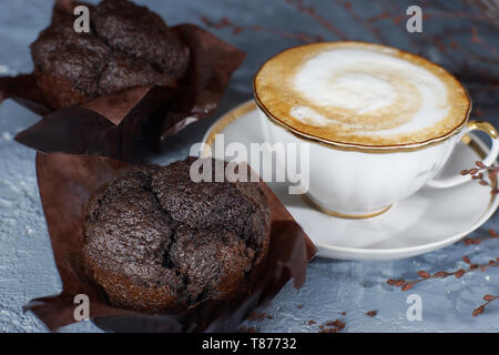 Eine Tasse Cappuccino steht auf einem grauen Tisch neben zwei schönen Schokolade Muffins Stockfoto