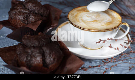 Eine Tasse Cappuccino Kaffee steht auf dem Tisch neben zwei schönen Schokolade Muffins Stockfoto