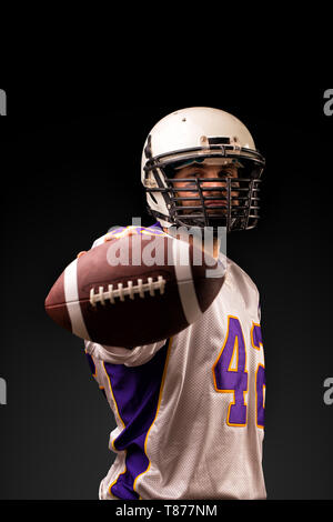 American Football Spieler, der den Ball in seinen Händen vor der Kamera. Konzept American Football, Motivation, schwarzer Hintergrund Stockfoto