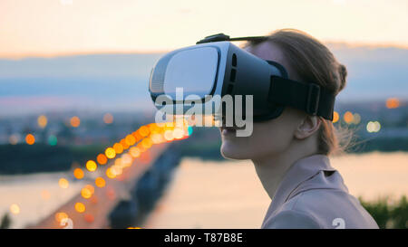 Frau verwendet virtuelle Realität Gläser in der Stadt nach Sonnenuntergang Stockfoto