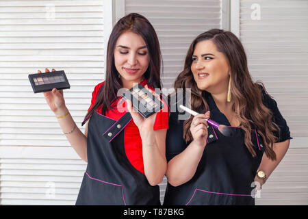 Professionelle Make-up-Künstler, visagistes zwei Mädchen in Uniform Lächeln, halten Lidschatten Paletten und Pinsel, auf weißem Hintergrund. Concept Plus größe Modell, b Stockfoto