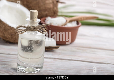 Hintergrund der Glasbehälter, Kokos, Kokosnussschalen, Öl in Ton Schüssel und Löffel auf weiße Holztisch Stockfoto
